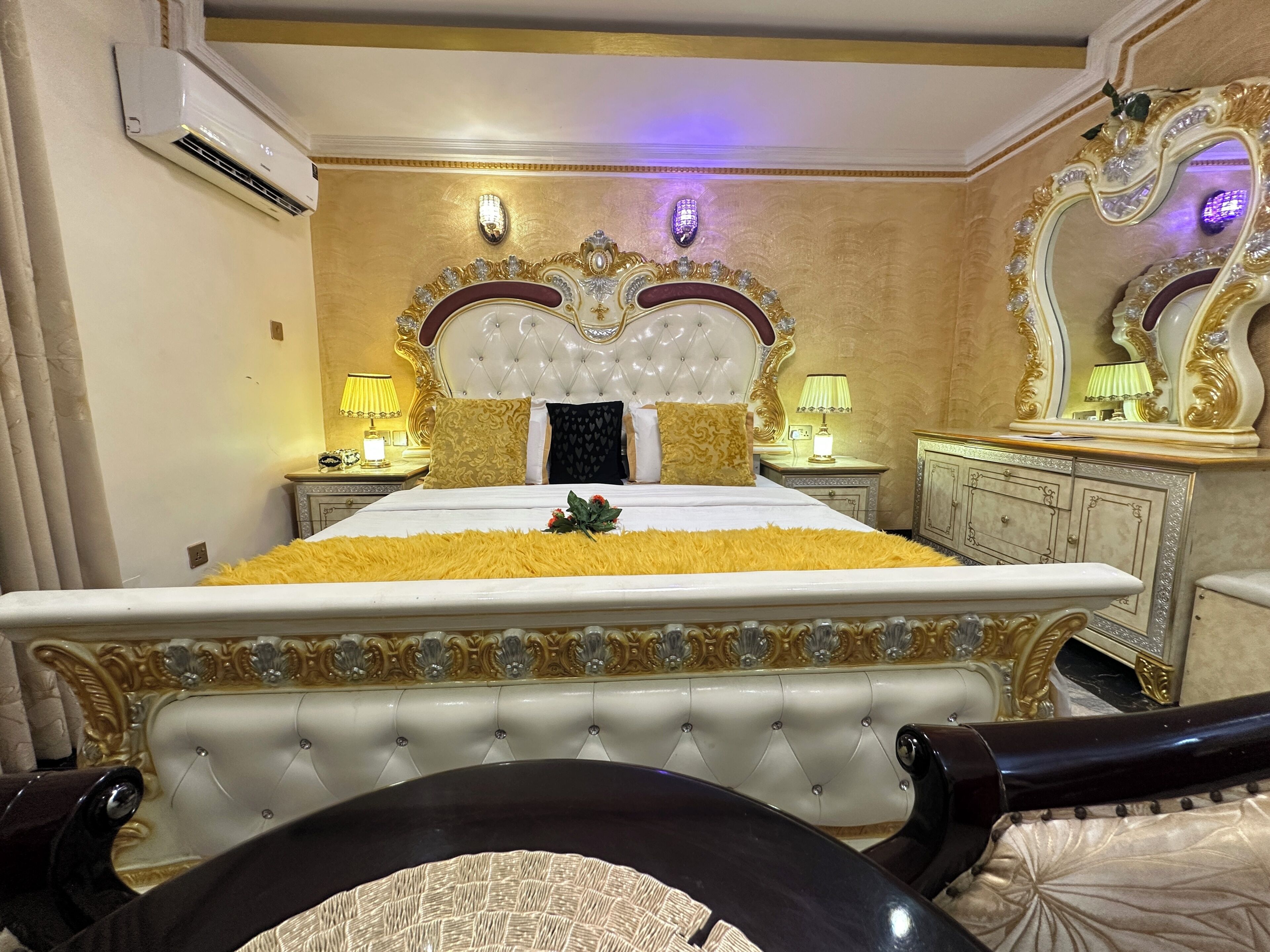 Un dormitorio lujoso con un cabecero capitonado, un espejo grande y mesas de noche ornamentadas.