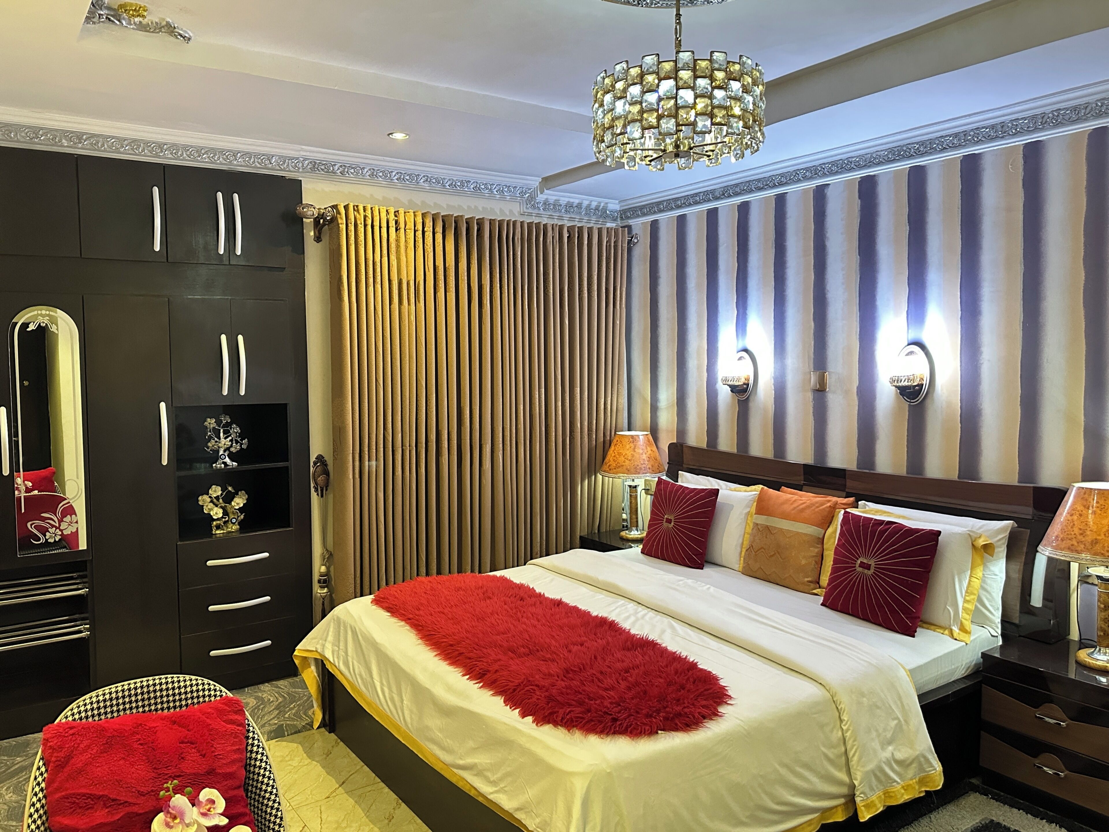 Une chambre d’hôtel avec un grand lit, une armoire, un miroir et un lustre.