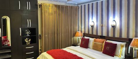 Une chambre d’hôtel avec un grand lit, une armoire, un miroir et un lustre.