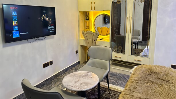 Ein modernes Wohnzimmer mit Flachbildfernseher, einem Essbereich mit rundem Tisch und Stühlen sowie einem großen Spiegel.
