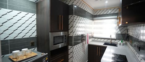 Una cocina moderna con un microondas Bosch, armarios oscuros, una ventana con persianas y un ventilador de techo.