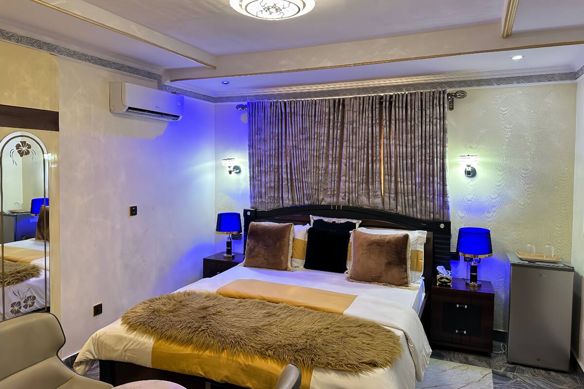 Quarto de hotel com uma cama grande, uma escrivaninha, uma cadeira, um espelho e um pequeno frigorífico.