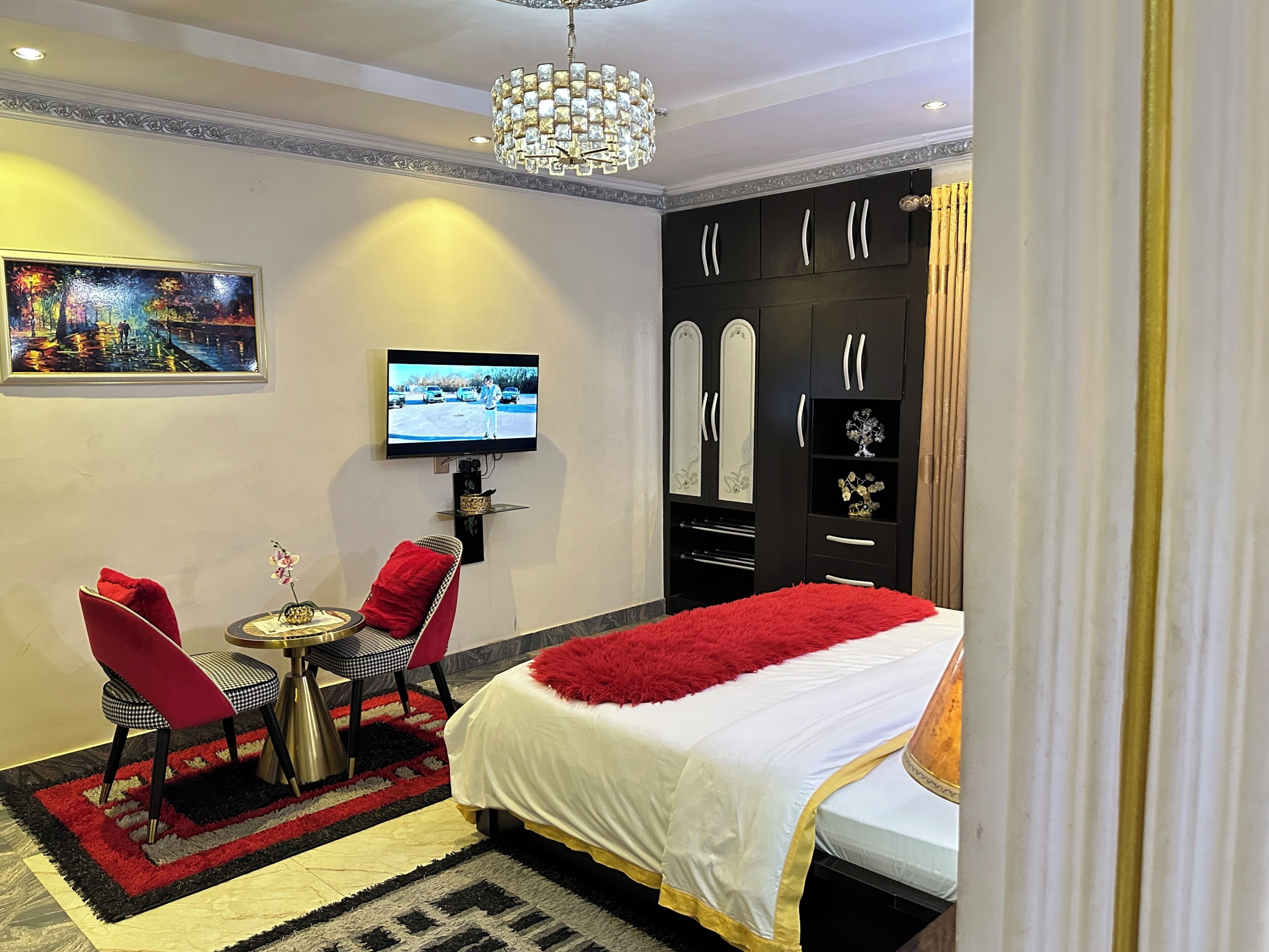 A hotel room with a bed, a TV, a desk with a chair, and a painting on the wall.
