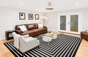 A modern living room with a brown leather sofa, a patterned armchair, a glass coffee table, and a black and white striped rug. - 2 Miles to OU • Quiet • Fenced Yard + Fire Pit (Norman)