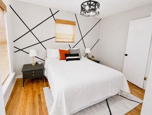 Ein Schlafzimmer mit Bett, Nachttischen, einer Lampe, einem Fenster mit Jalousien und einer Tür.