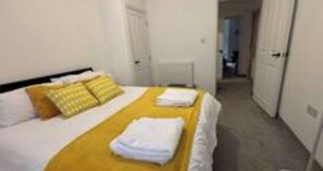 A hotel room with a bed, a bedside table, and a door leading to another room. - 1BR Parkside Apt Contractors & Families w/Parking (West Northamptonshire)