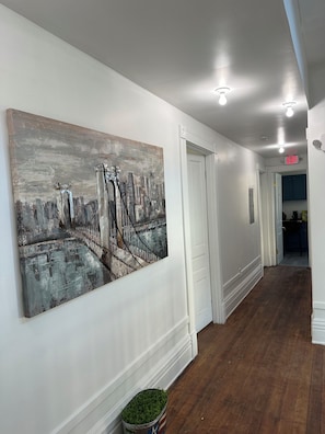 A hallway with a large abstract painting, white walls, wooden flooring, and an exit sign. - Cozy 2-bedroom townhome in pleasant Louisville with AC (Louisville)