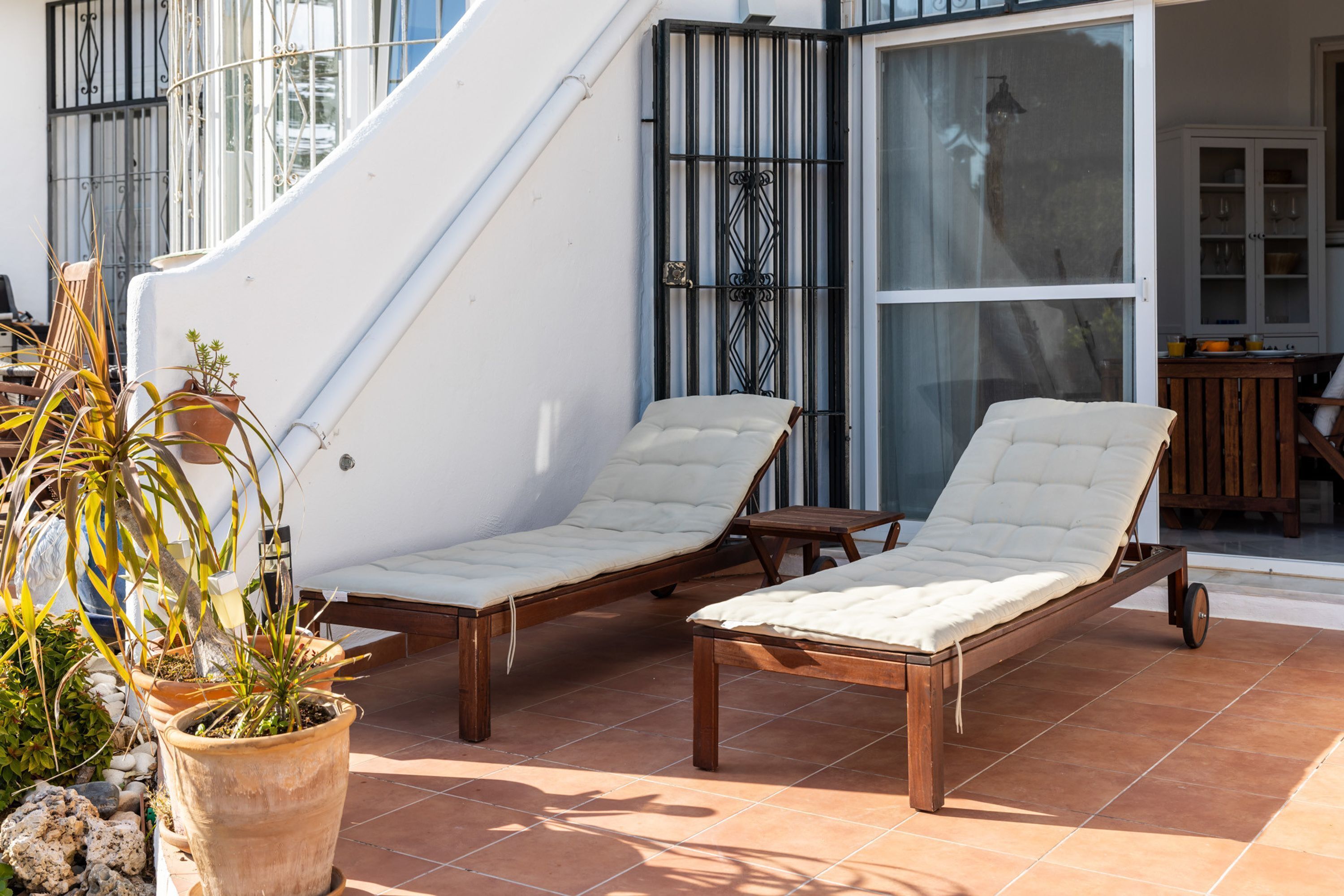 Una terrazza con due poltrone, un muro bianco, un cancello in metallo e piante in vaso.