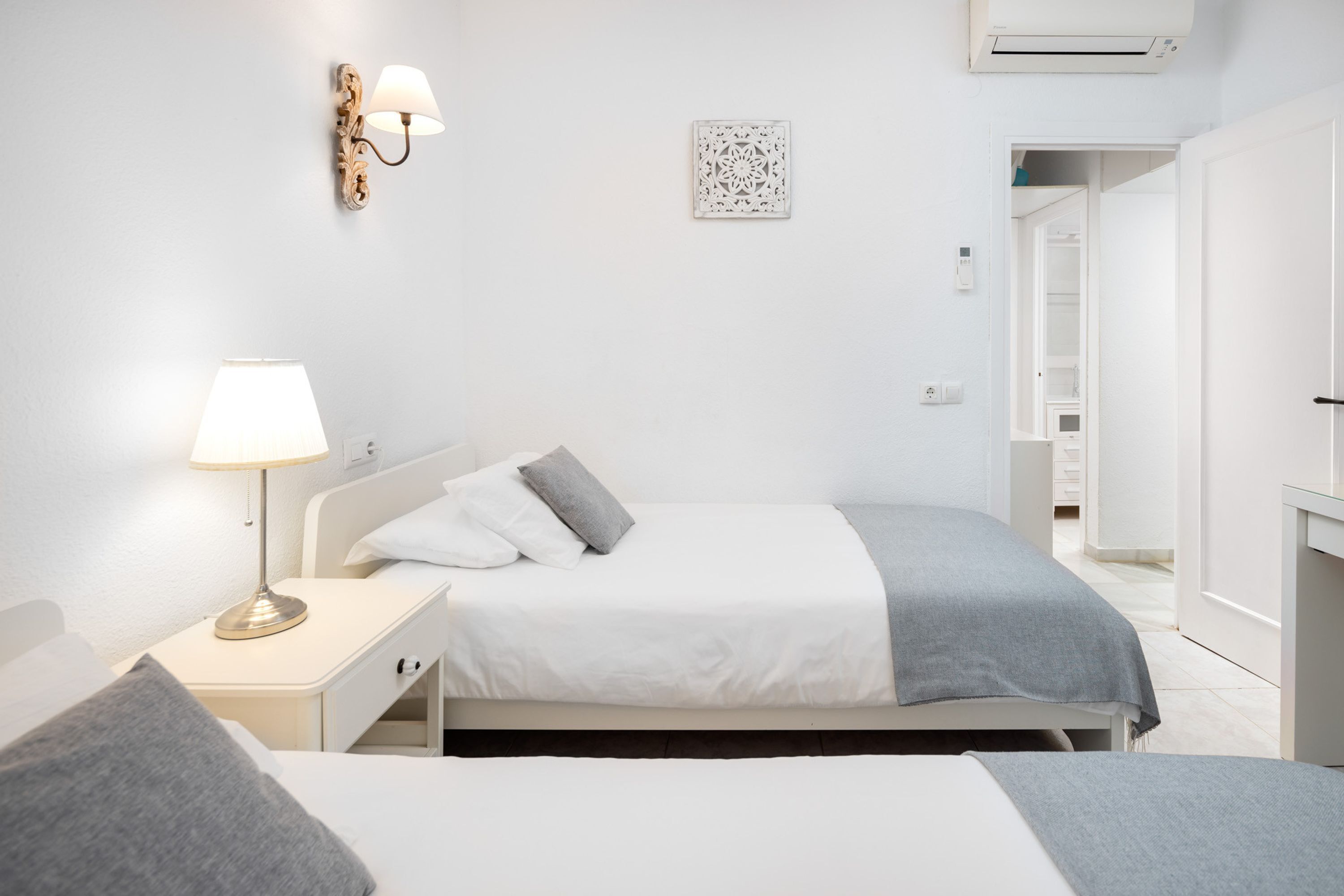 Een hotelkamer met een bed, nachtkastje, lamp en een wandairconditioner.