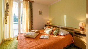 A hotel room with a bed, a bedside table with a lamp, a window with curtains, and a view of greenery outside. - One-bedroom apartment Casa Vidasca 103 with the pool and the private balcony (Novalja)