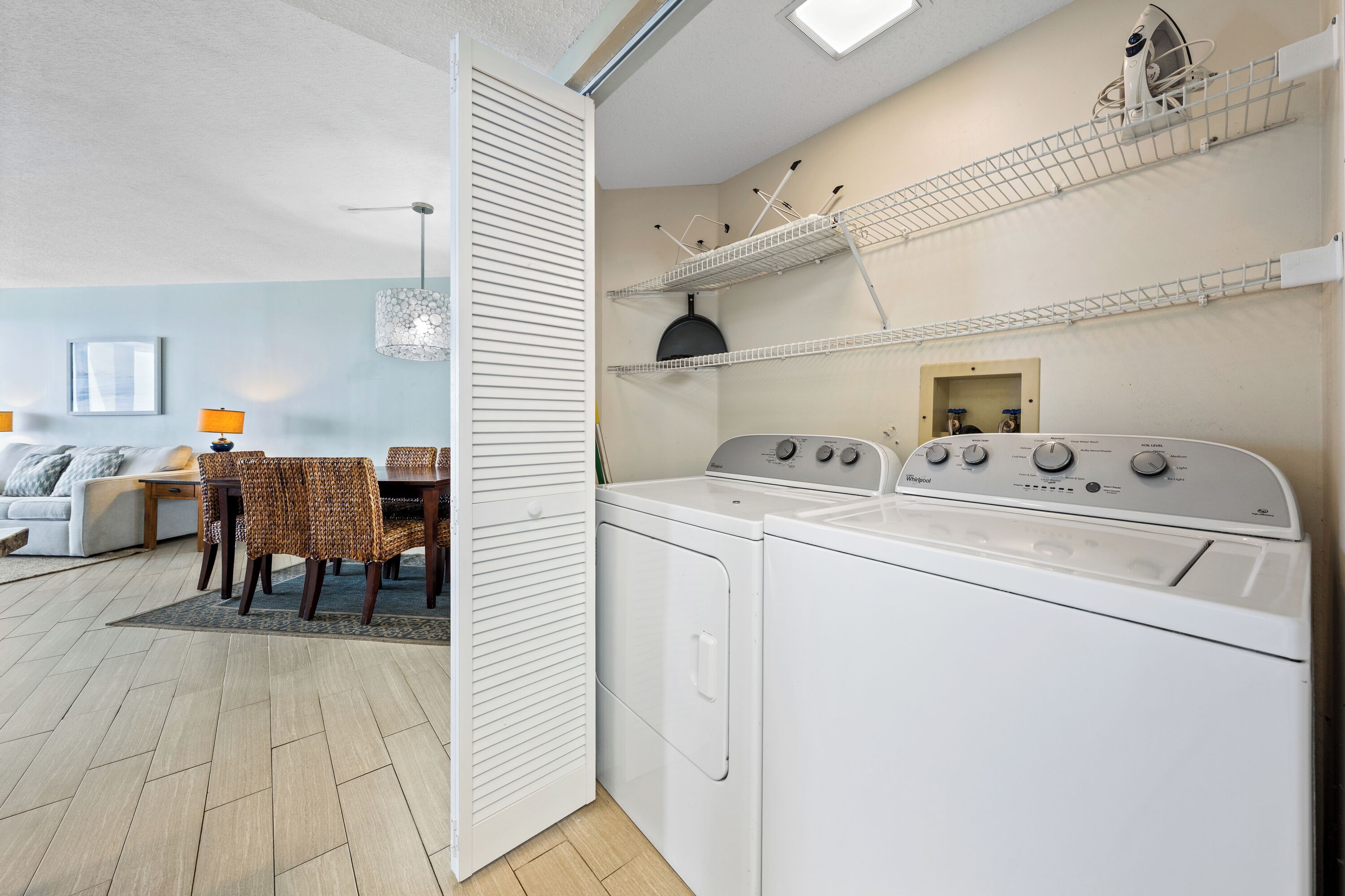 A compact laundry area with a washer and dryer, a dining table with chairs, and a kitchen shelf.