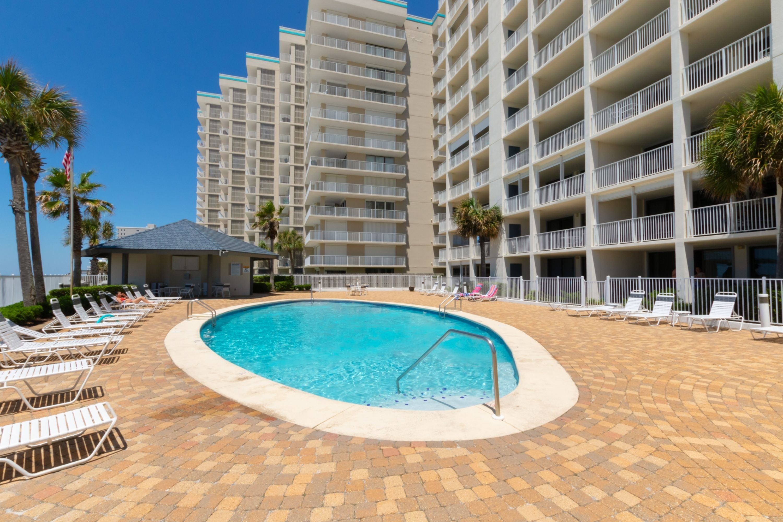 A swimming pool with lounge chairs and a building with multiple balconies in the background.
