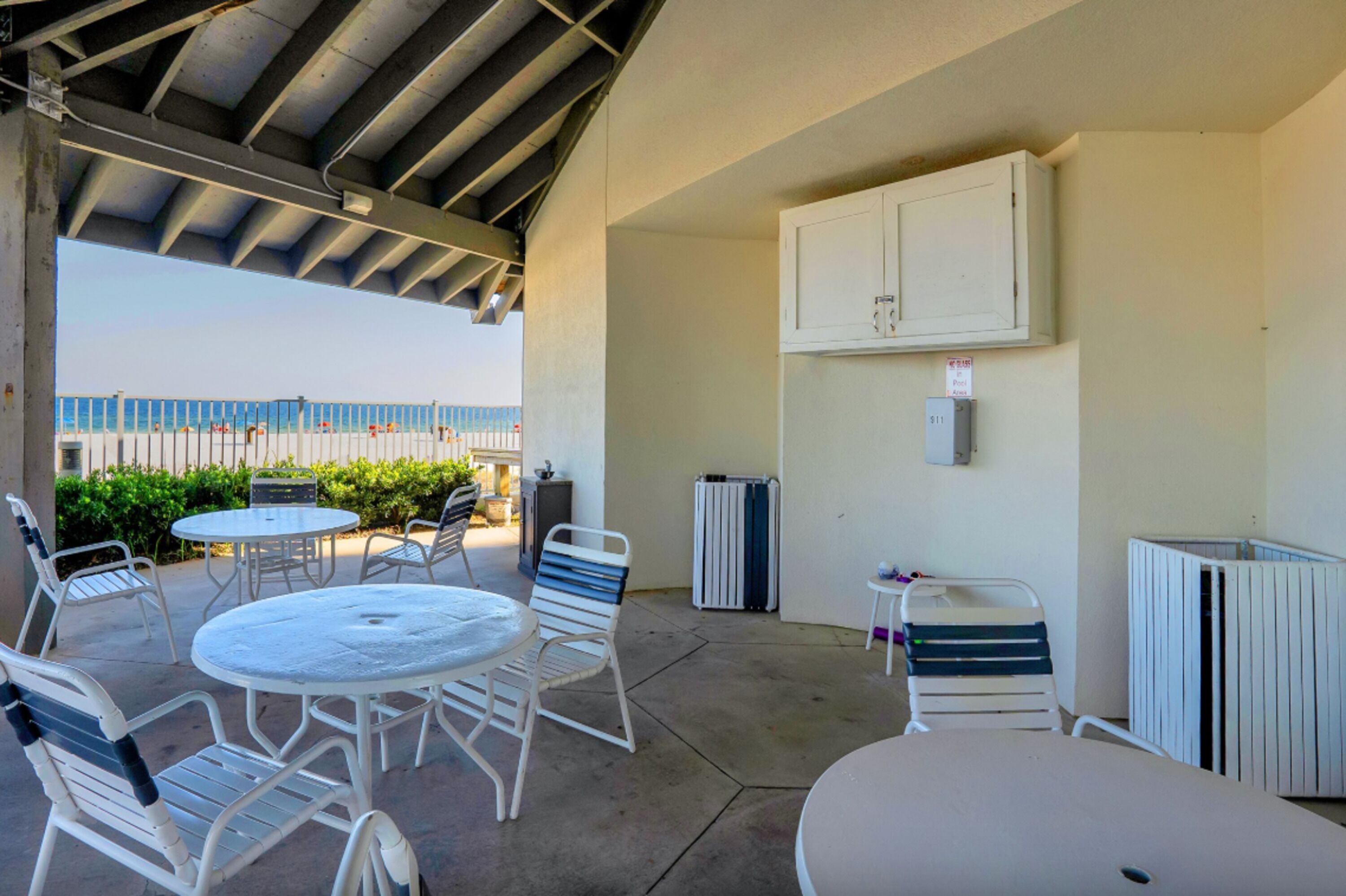 A covered outdoor patio with tables and chairs, a white cabinet, and a radiator.