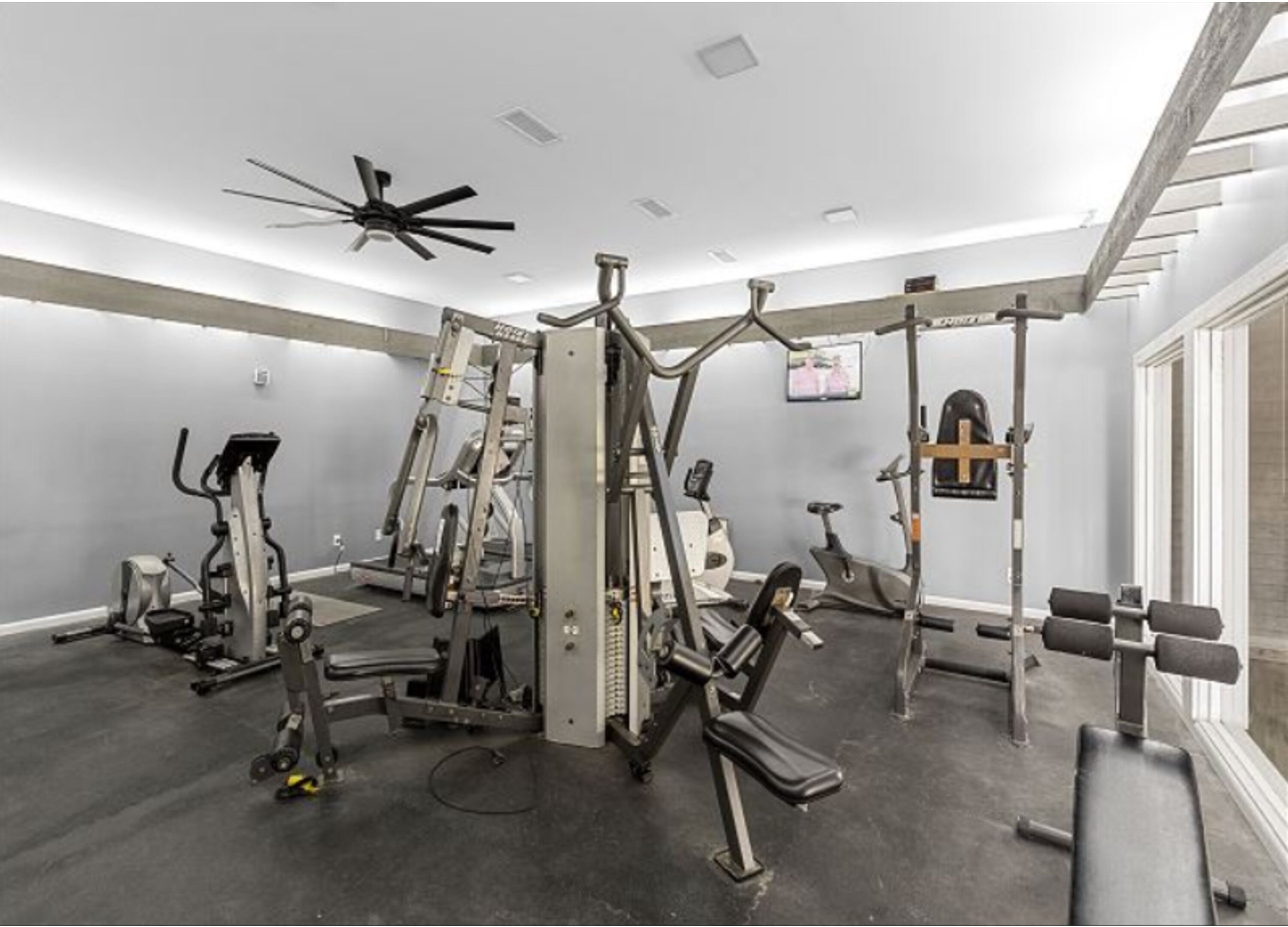 A gym with various exercise equipment, a ceiling fan, and a television on the wall.