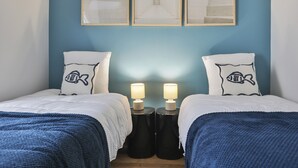 Habitación de hotel con dos camas, una pared azul y tres cuadros enmarcados encima de las camas.