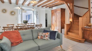 Una sala de estar con sofá, vigas de madera, zona de comedor y una escalera.
