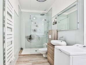 Ett modernt badrum med en duschkabin i glas, en toalett, ett handfat och en inbyggd tvättmaskin.