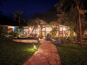 A well-lit outdoor area with a pathway leading to a building with large windows and a covered patio area. - Xalli Hotel (Altagracia)