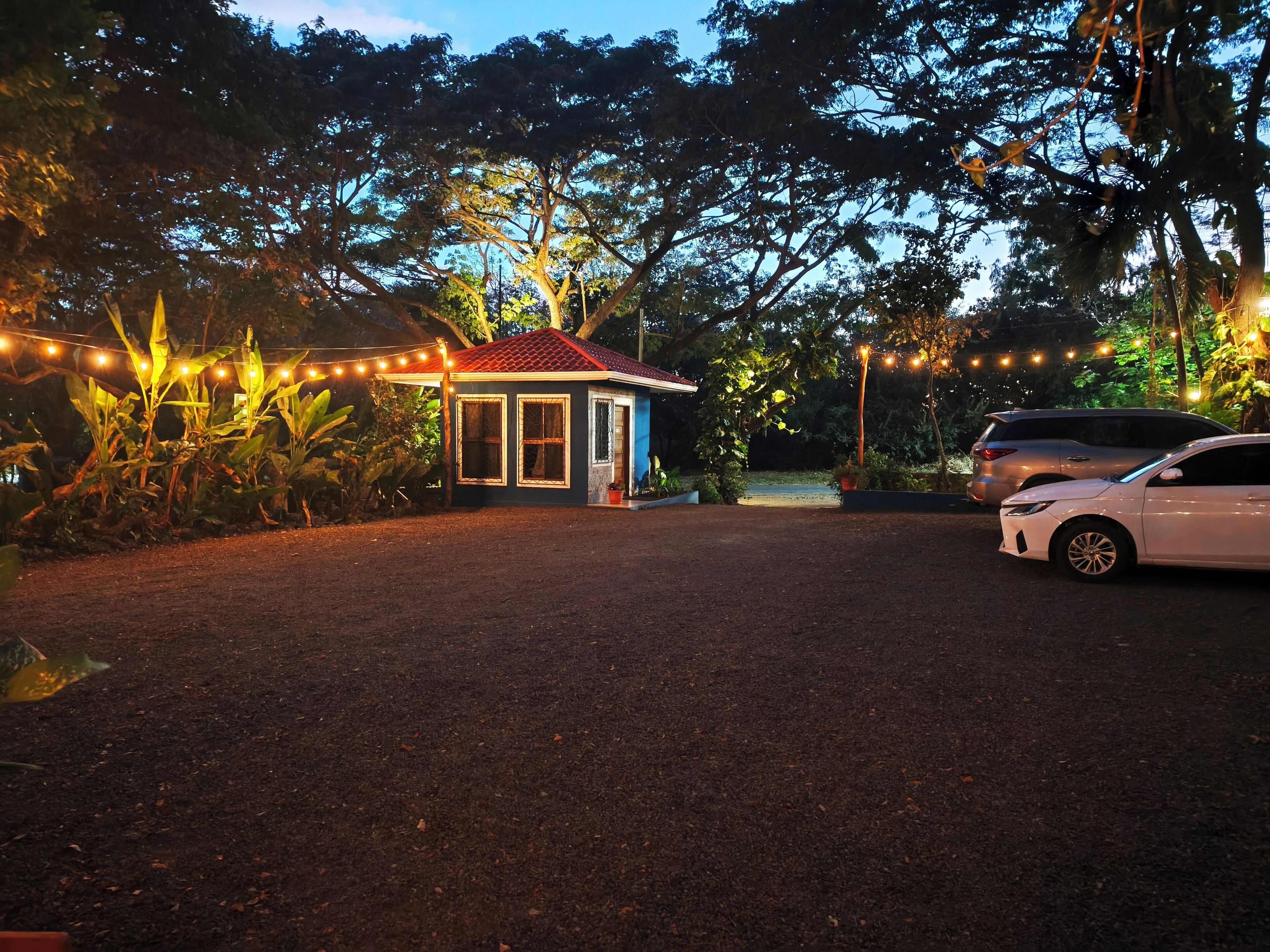 A small house with a red roof and a porch, surrounded by trees and string lights.