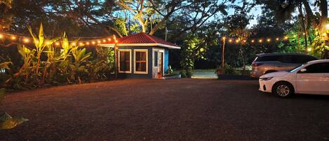 A small house with a red roof and a porch, surrounded by trees and string lights.