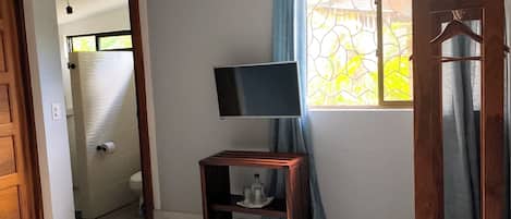 Una camera da letto con un letto, una TV su un mobile, un condizionatore, una finestra con tende e una porta in legno.