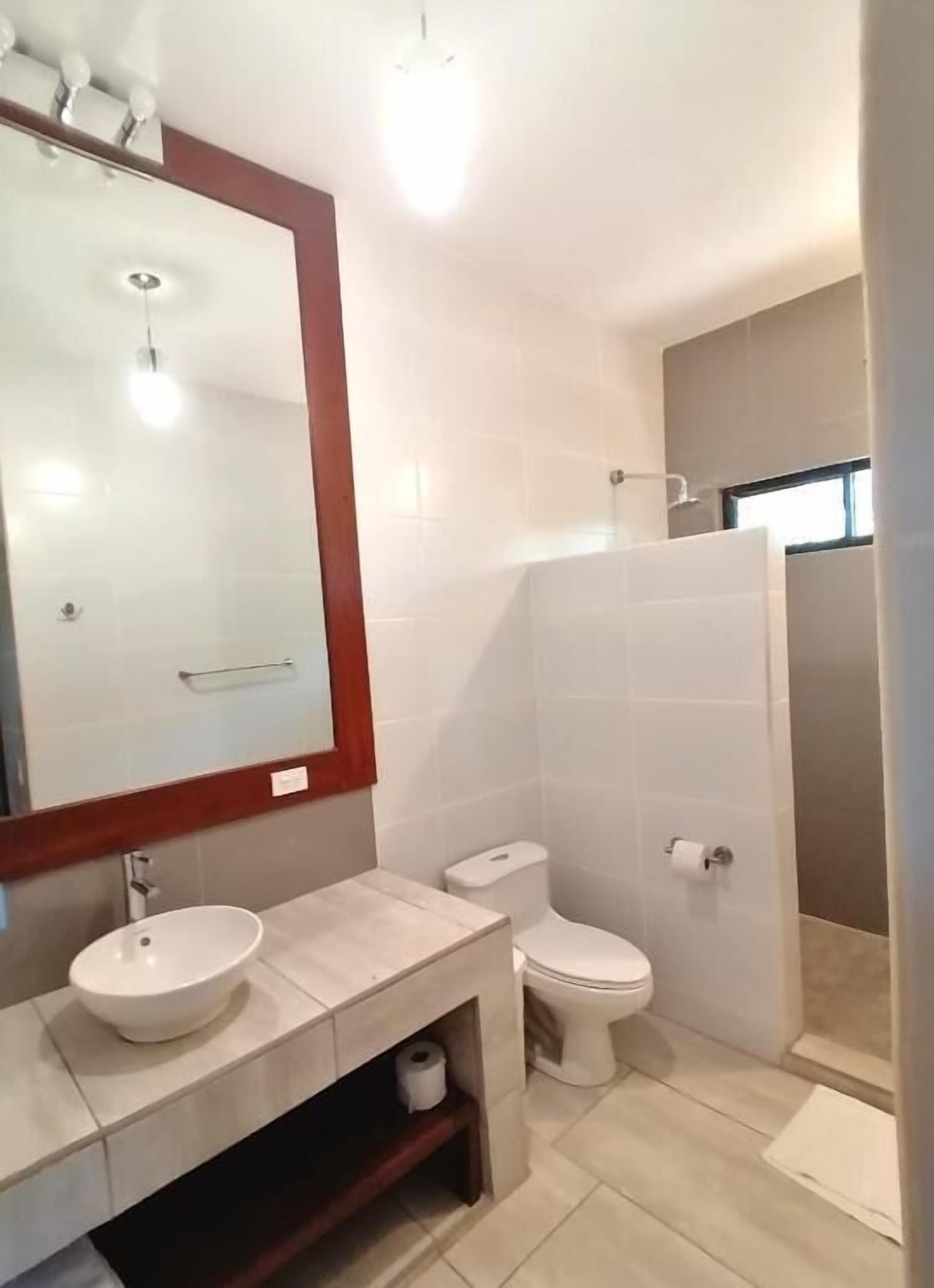 A modern bathroom with a large mirror, a sink, a toilet, and a shower.