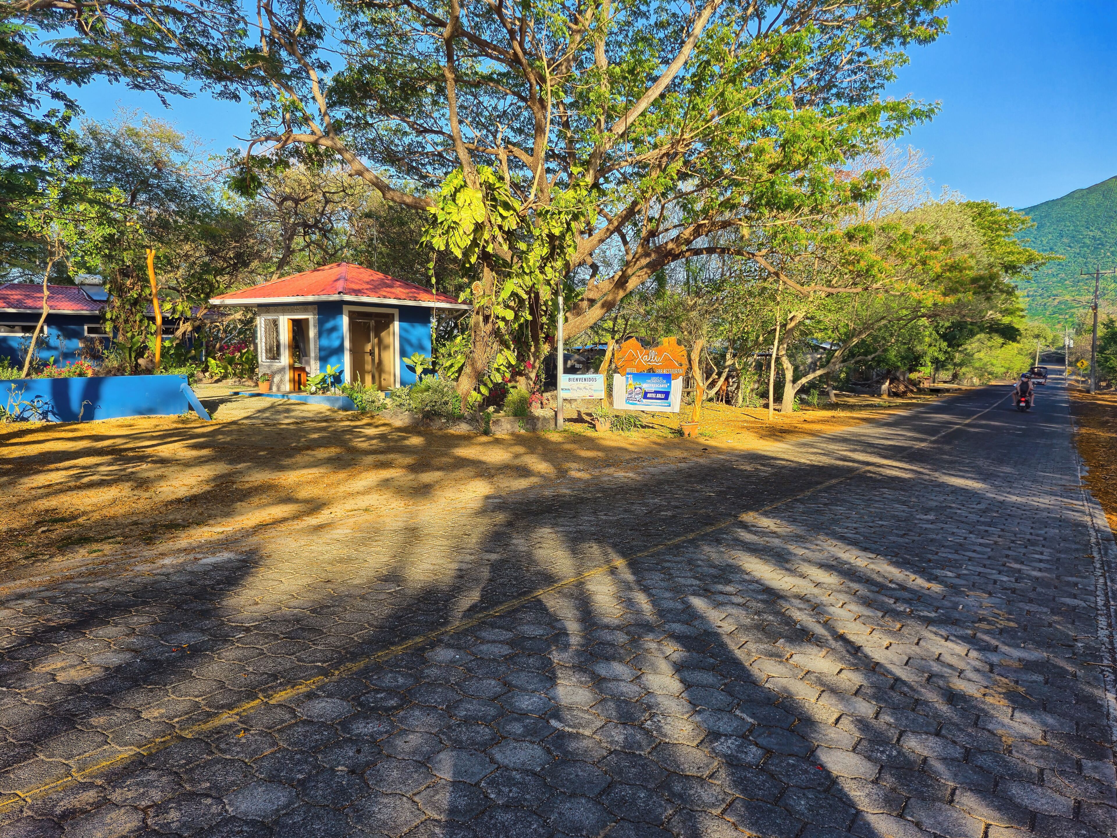 A paved road with a signboard, a building with a red roof, and trees.