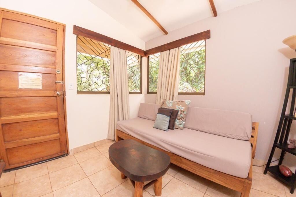 Une pièce avec une porte en bois, un canapé avec des coussins, une petite table et une fenêtre avec des rideaux.