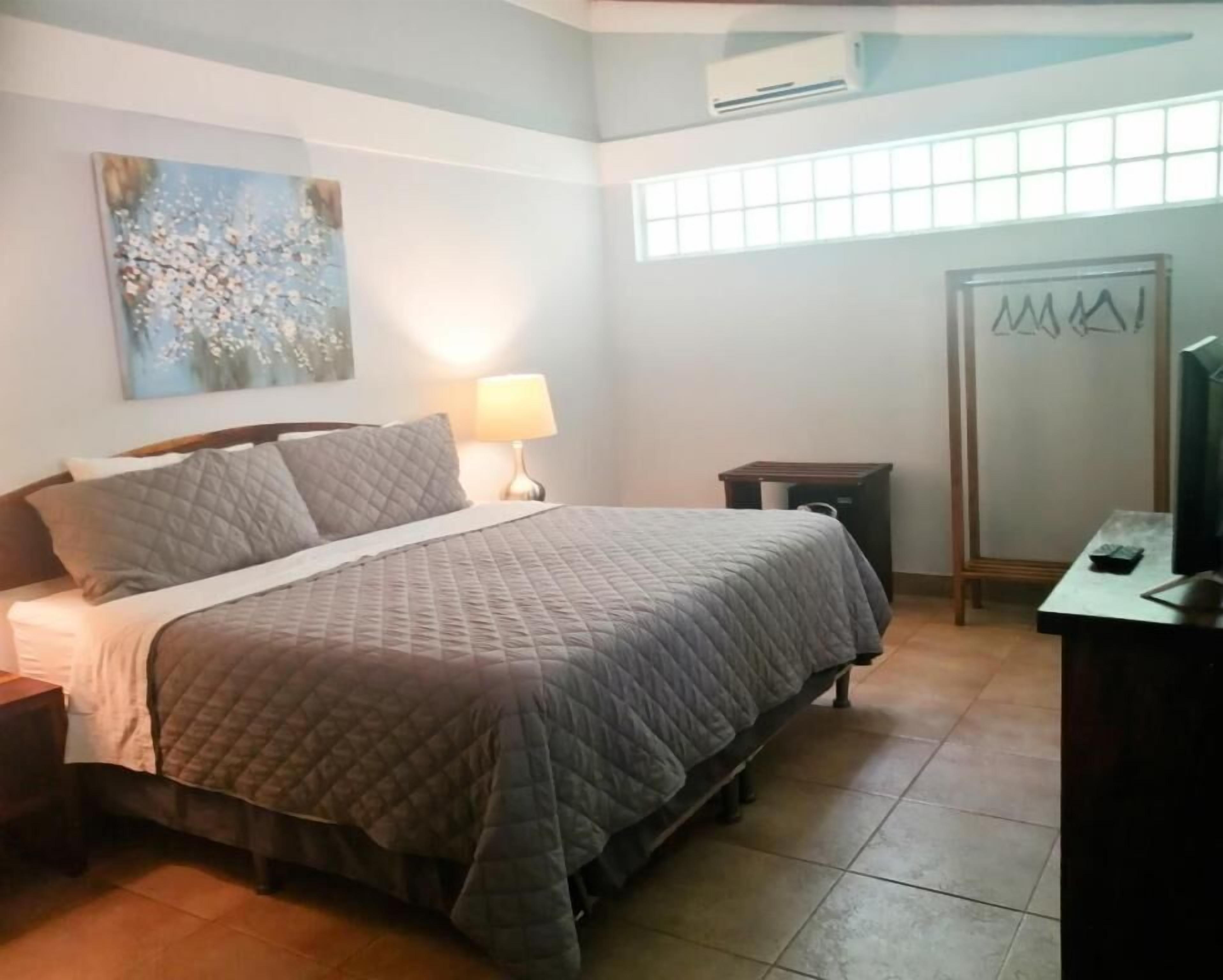 Une chambre à coucher comprenant un lit, une table de chevet, une lampe, une commode et un miroir.