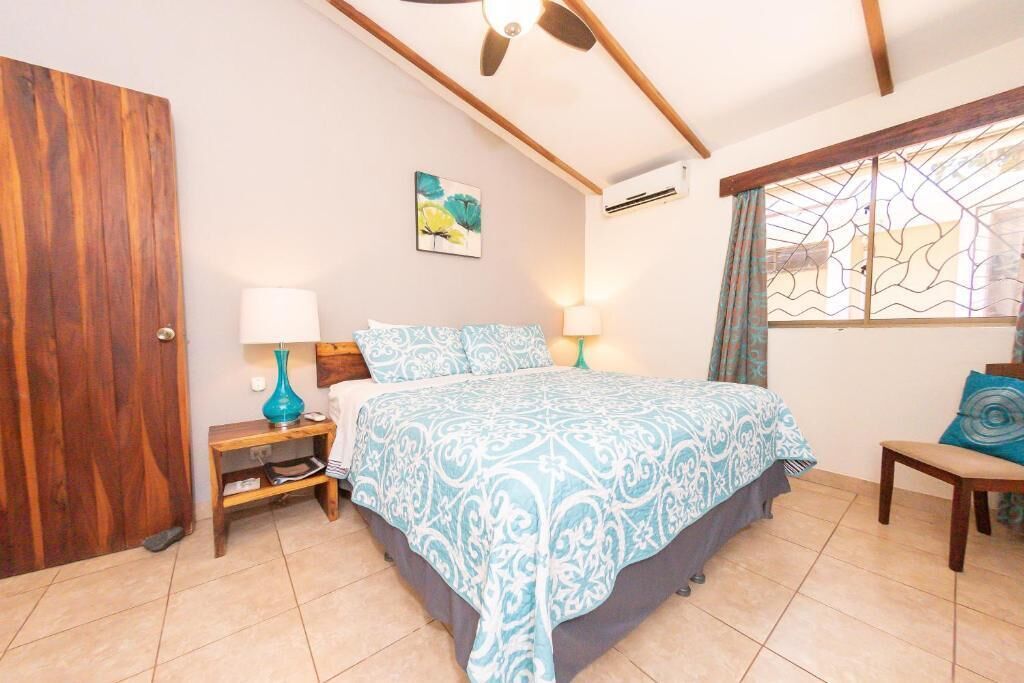 Une chambre à coucher avec un lit, des lampes de chevet, une porte en bois, un climatiseur mural et une fenêtre avec des rideaux.