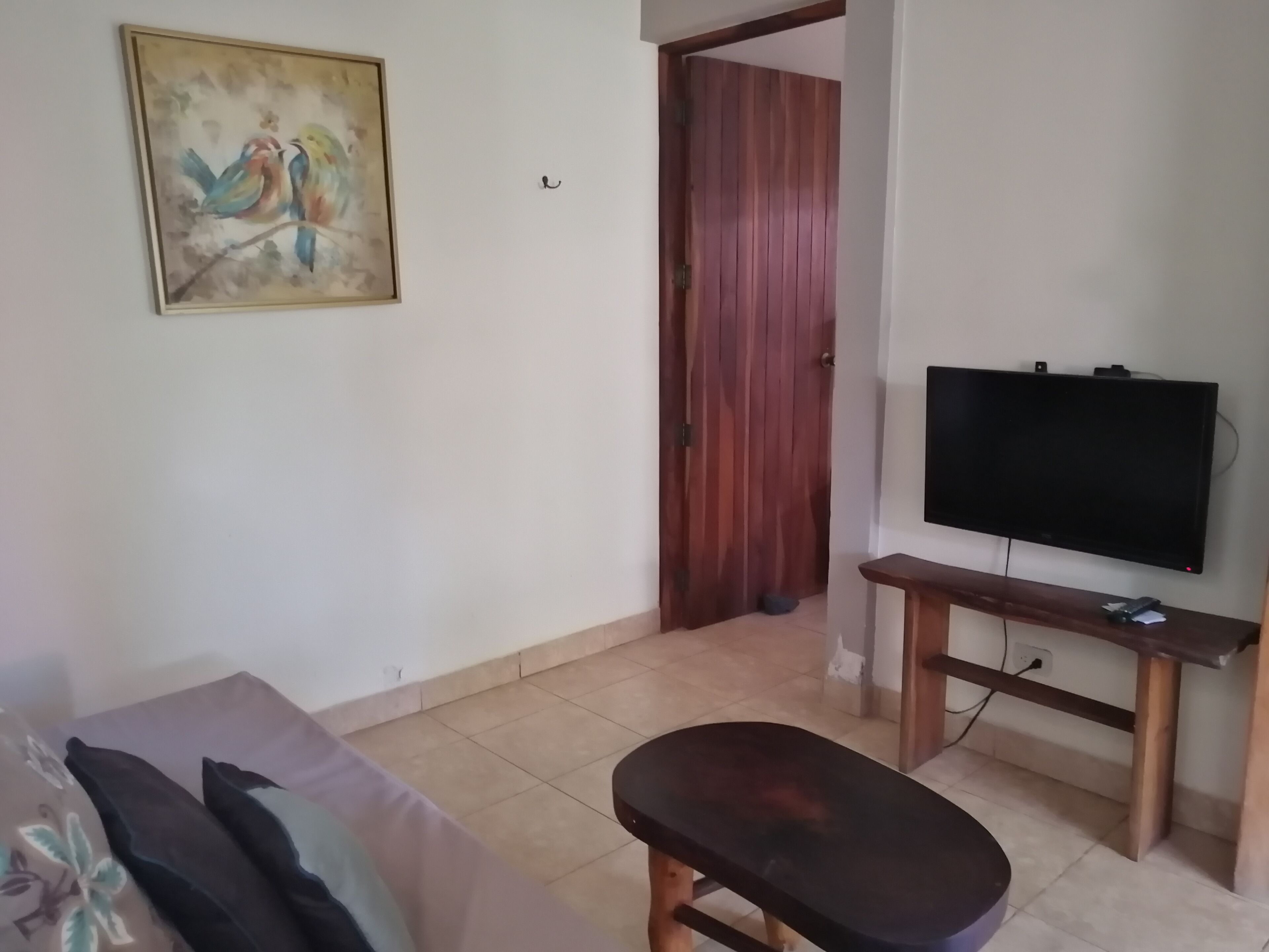 A living room with a sofa, a bench, a television on a stand, a wooden door, and a painting on the wall.