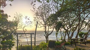 Un patio empedrado de piedra con una pérgola de madera, un banco y una hamaca con vistas a una playa.