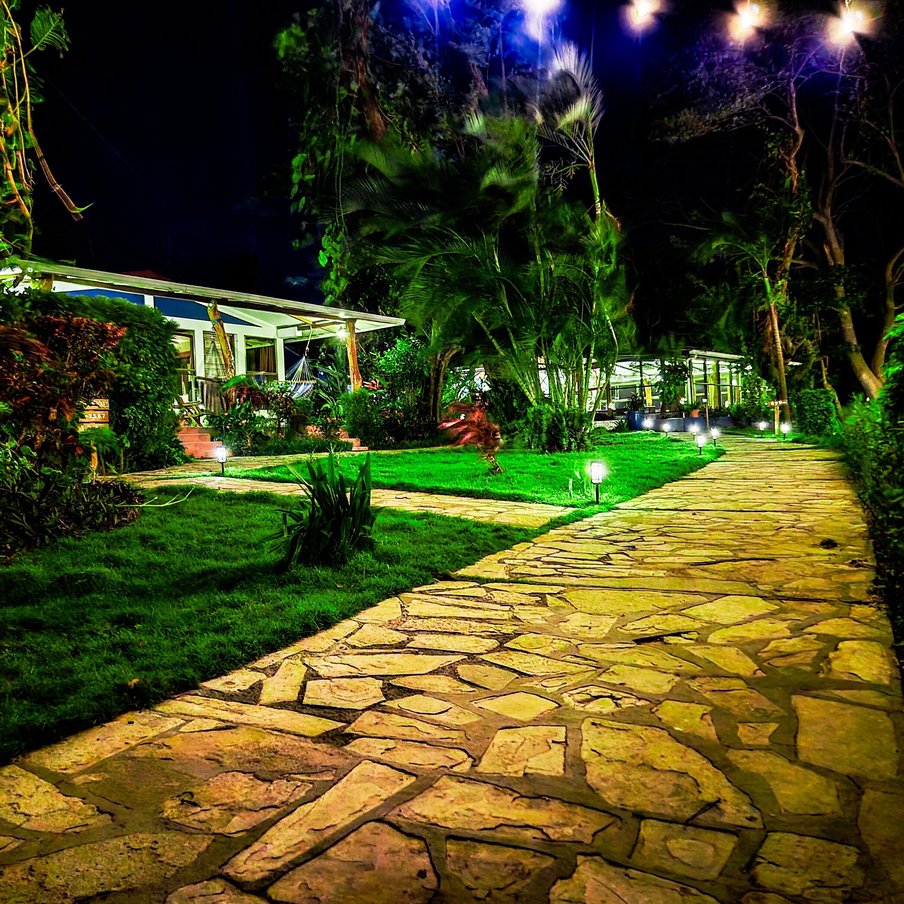 A stone pathway leading to a building with a covered outdoor area, surrounded by greenery.