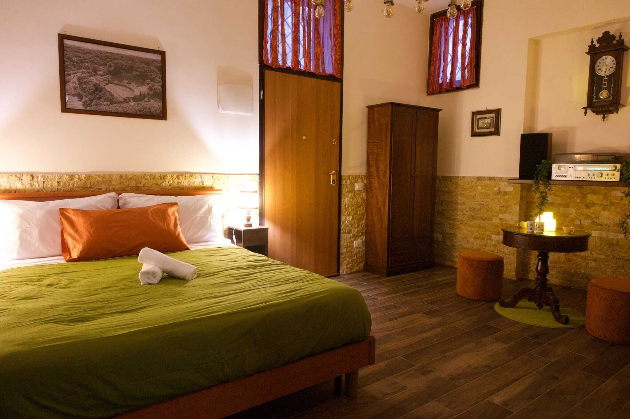 A hotel room with a bed, a wardrobe, a table with a radio, and a clock on the wall.