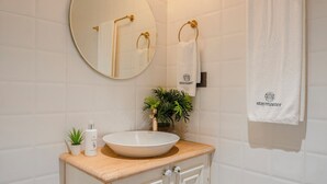 Une salle de bain avec un miroir rond, un lavabo doté d’un plan de travail en bois, un porte-serviettes avec une serviette blanche et une petite plante en pot.