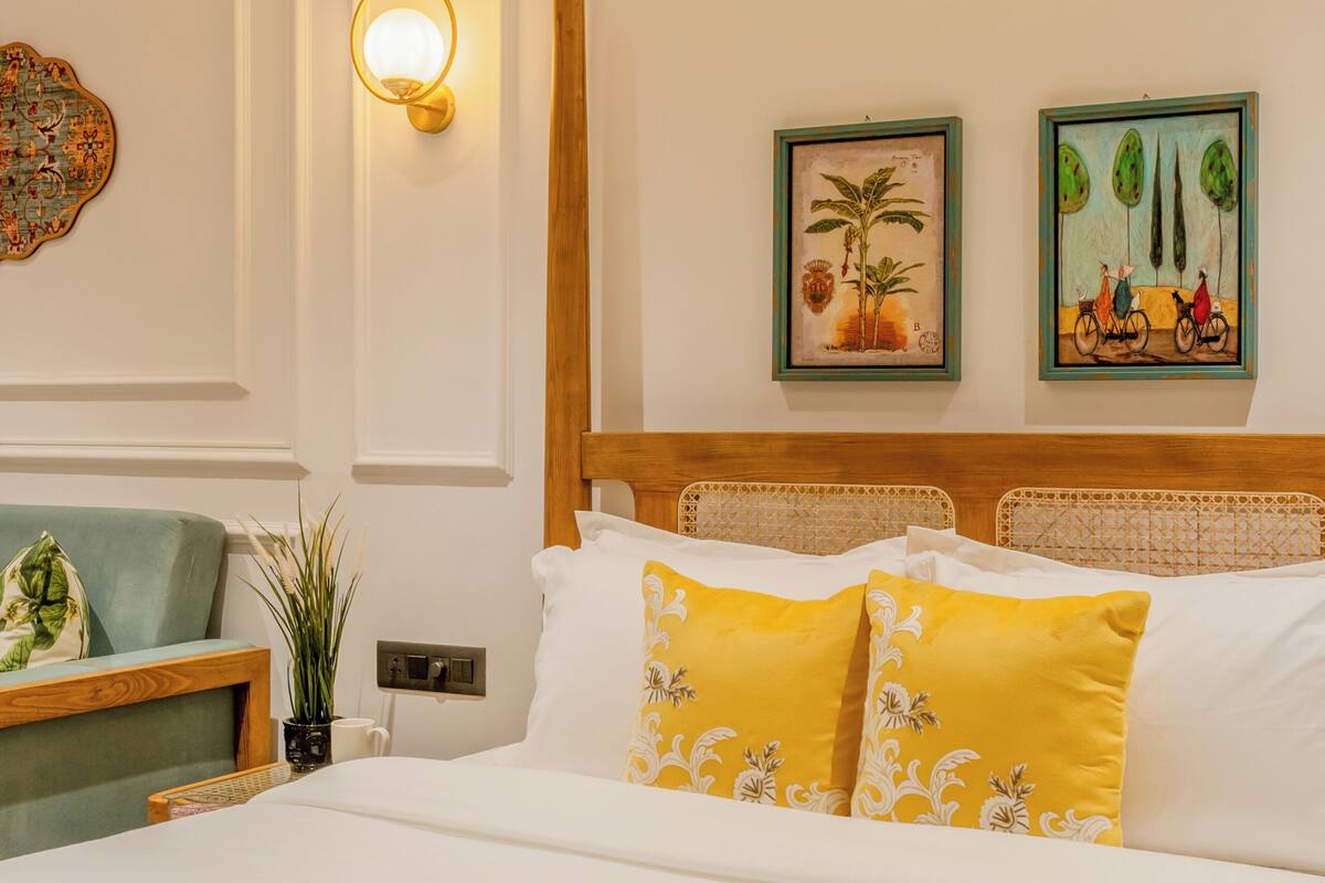 A neatly arranged hotel room with a bed, a nightstand, a wall-mounted light fixture, and two framed artworks.