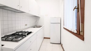 Ett kompakt kök med vita skåp, en gasspis, en diskho och ett kylskåp.
