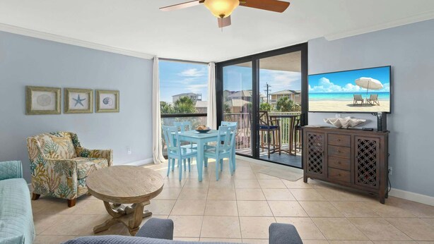 Un salon doté d’un ventilateur de plafond, une table à manger avec des chaises, un canapé, un téléviseur posé sur un meuble et un balcon avec vue.