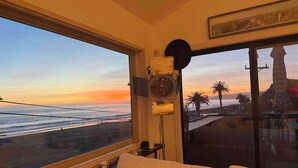 Una stanza con una grande finestra vista spiaggia al tramonto, un letto e un altoparlante a parete.