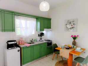 A compact kitchen with green cabinets, a coffee maker, a kettle, and a dining area with a table and chairs. - Spiros Studio by Hestia Travel just 550m from Roda Beach. (Roda)