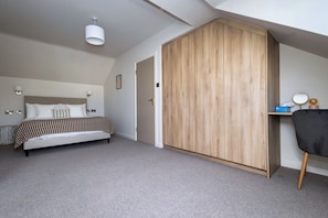 Un dormitorio con cama, armario, escritorio con silla, y lámpara fijada a la pared.