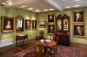 A dining room with a wooden table, chairs, a red upholstered chair, a mirror, and framed portraits on the walls. - The George and Dragon Hotel (Sudbury)