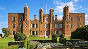 A large brick building with multiple towers and a well-manicured garden in front. - The George and Dragon Hotel (Sudbury)