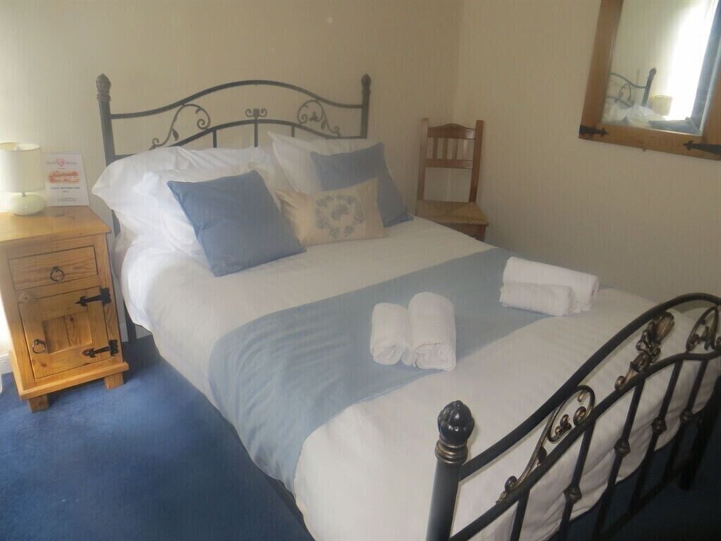Een netjes opgemaakt bed met kussens, een houten nachtkastje met een lamp en een stoel.