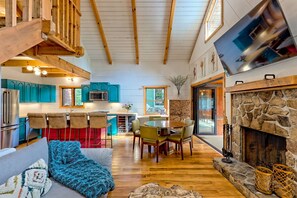 A spacious living area with a high ceiling, wooden beams, a fireplace, and a dining table with chairs.