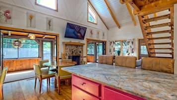 Une pièce spacieuse avec une grande table à manger en bois, une cheminée en pierre et un plafond haut avec des poutres apparentes.