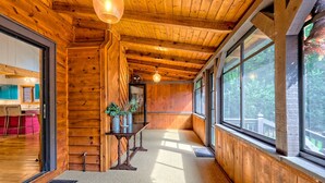 A wooden interior with a kitchen area, a dining table, and large windows.