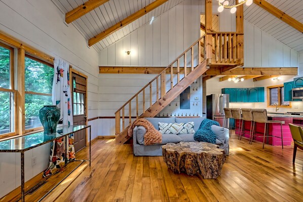 A spacious living area with a wooden staircase, a sofa, a coffee table, and a glass-top table with a vase.