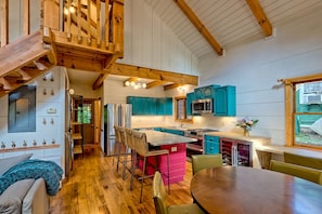 A spacious kitchen with wooden beams, teal cabinets, and a dining area with a wooden table and chairs.