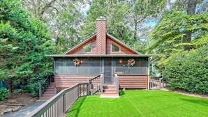 A cabin with a wooden exterior, a chimney, a front porch, and a well-maintained lawn.